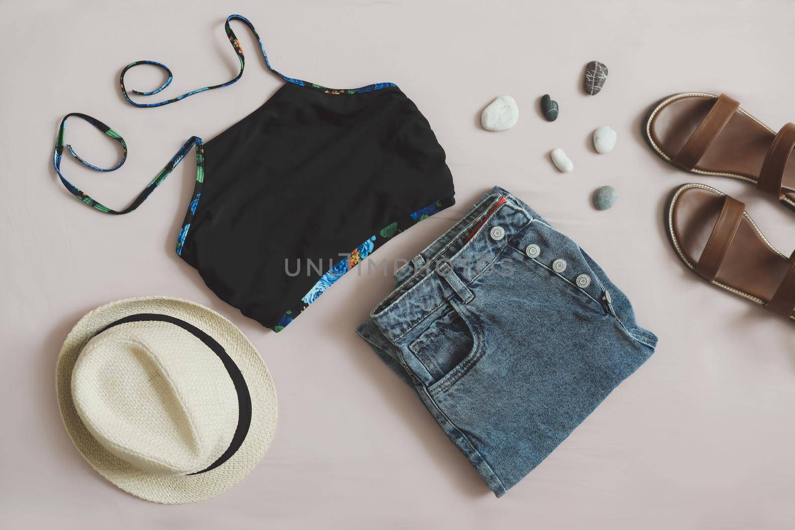 flat lay composition with female top, denim shorts, sandals and a wicker rattan bag on beige background top view.