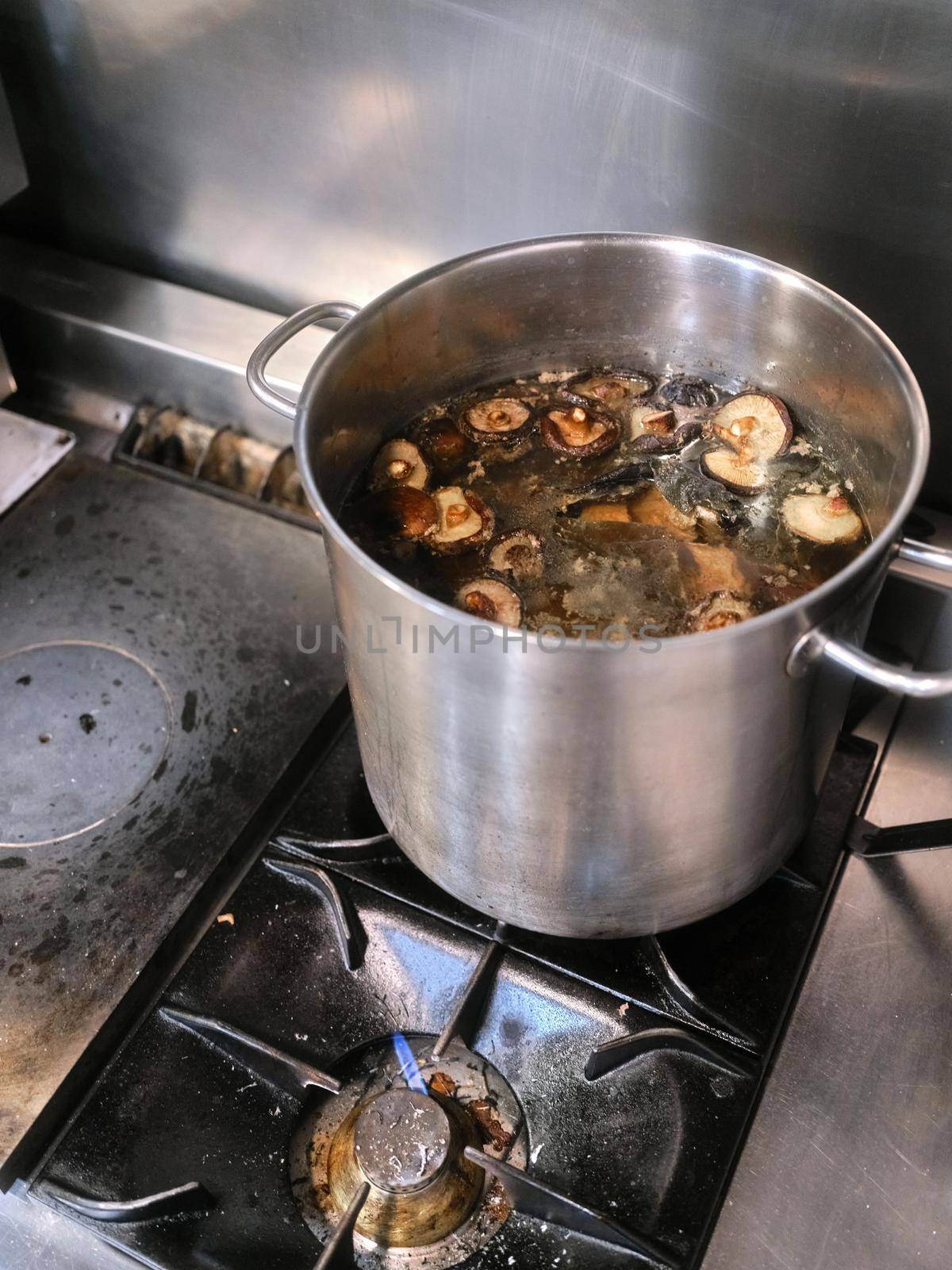 Vertical photo of a cooker of a restaurant with a pot of boiling mushrooms in it