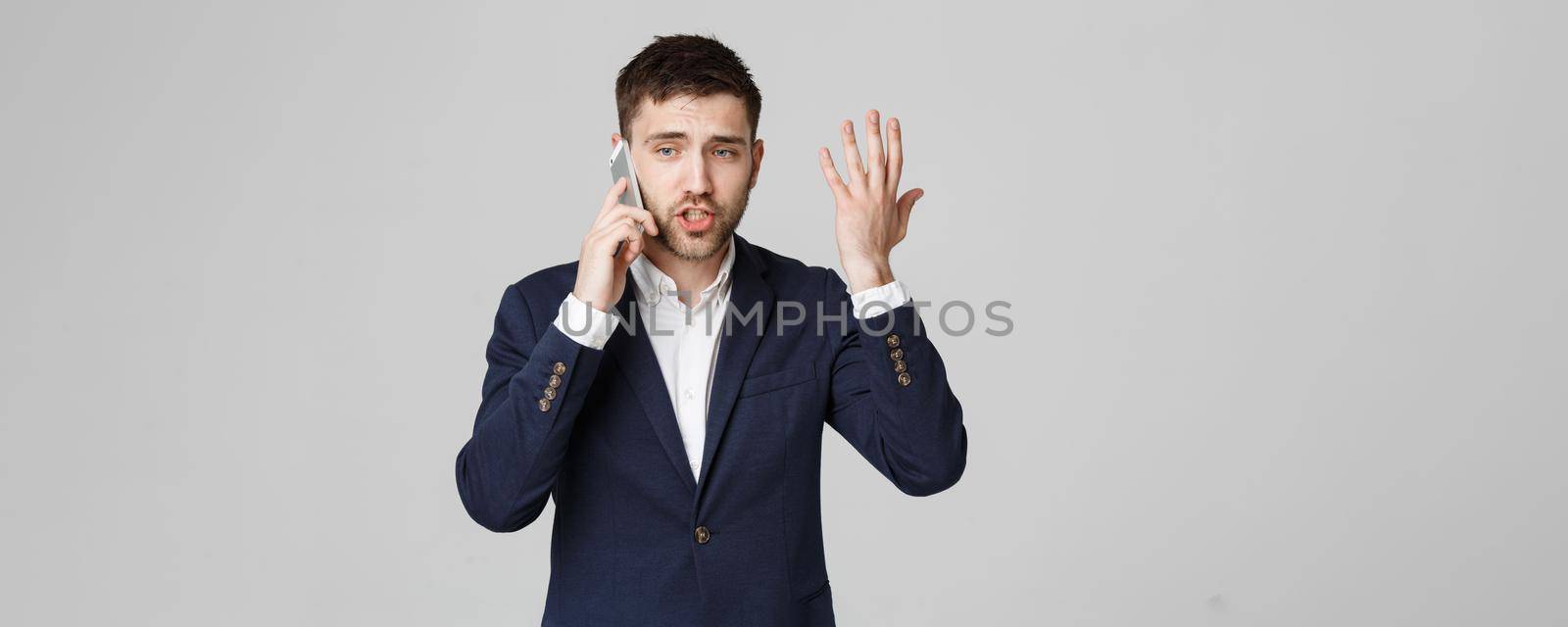 Business Concept - Portrait young handsome angry business man in suit talking on phone looking at camera. White background.