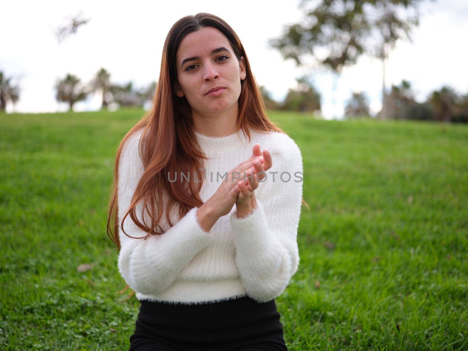 Front view of a young woman in the park condescendingly clapping to camera. Concept of emotions.