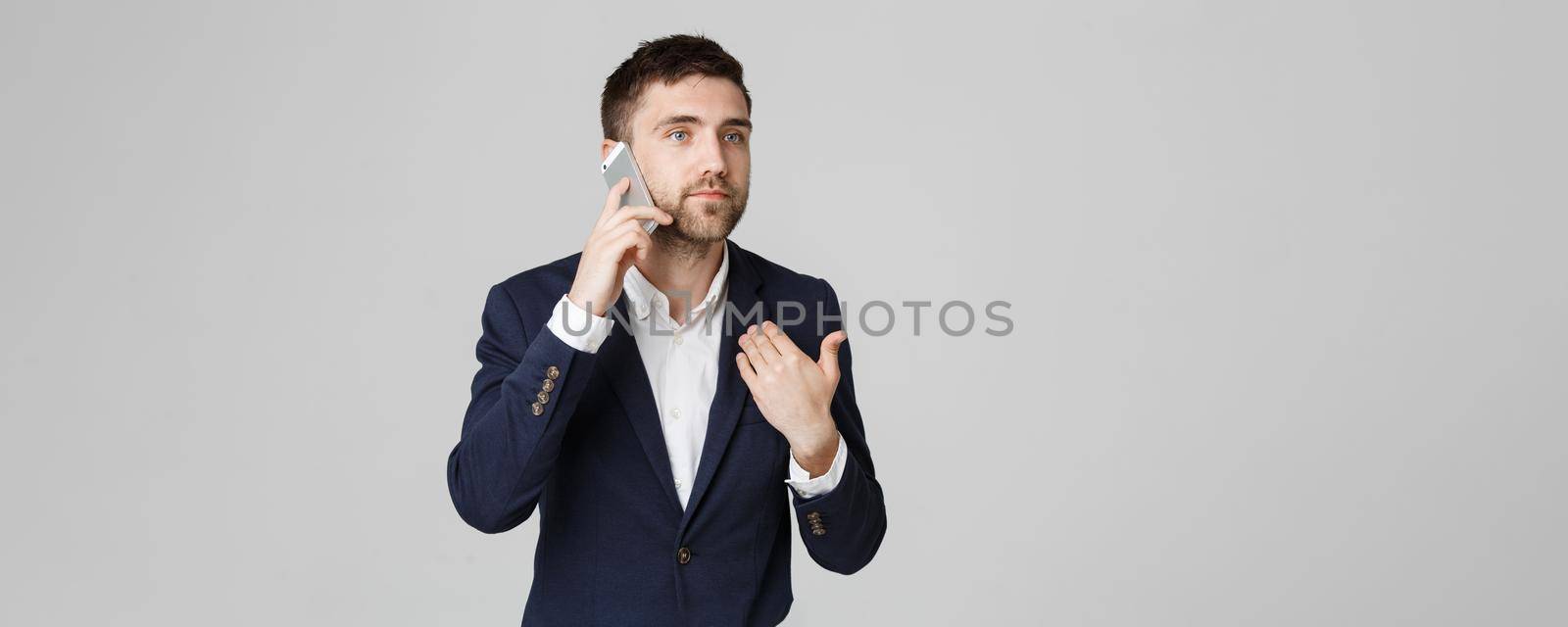 Business Concept - Portrait young handsome angry business man in suit talking on phone looking at camera. White background.