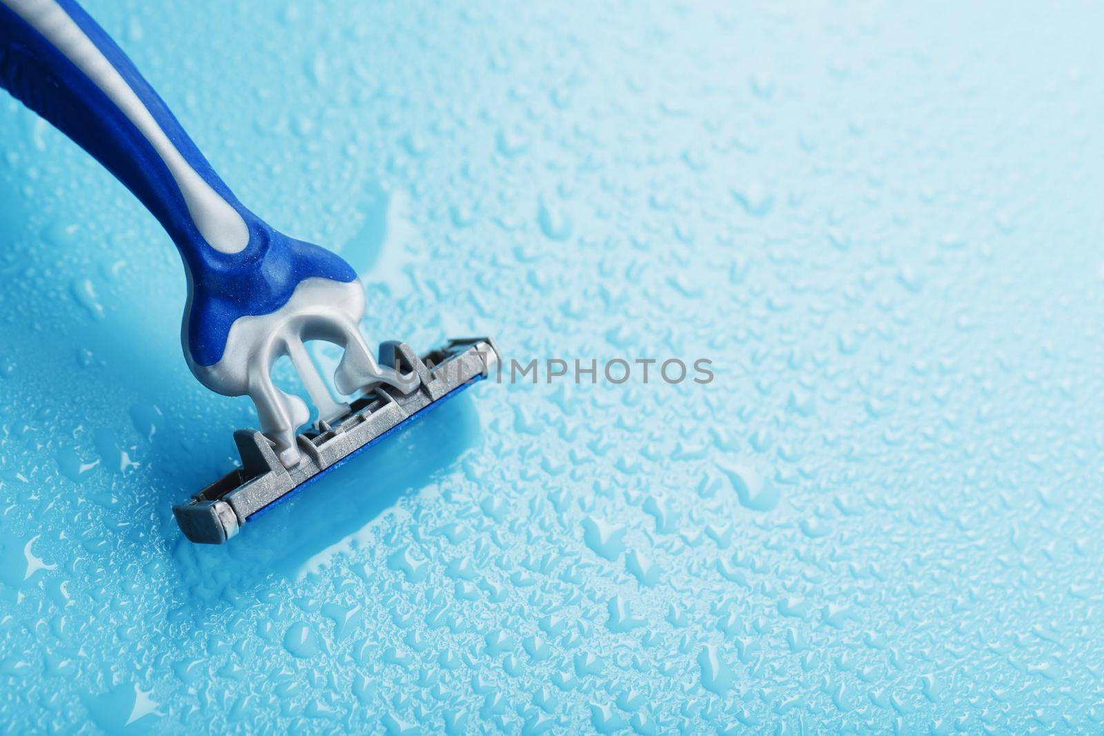 Shaving machine with three blades on a blue background with water drops in close-up. The concept of purity and freshness