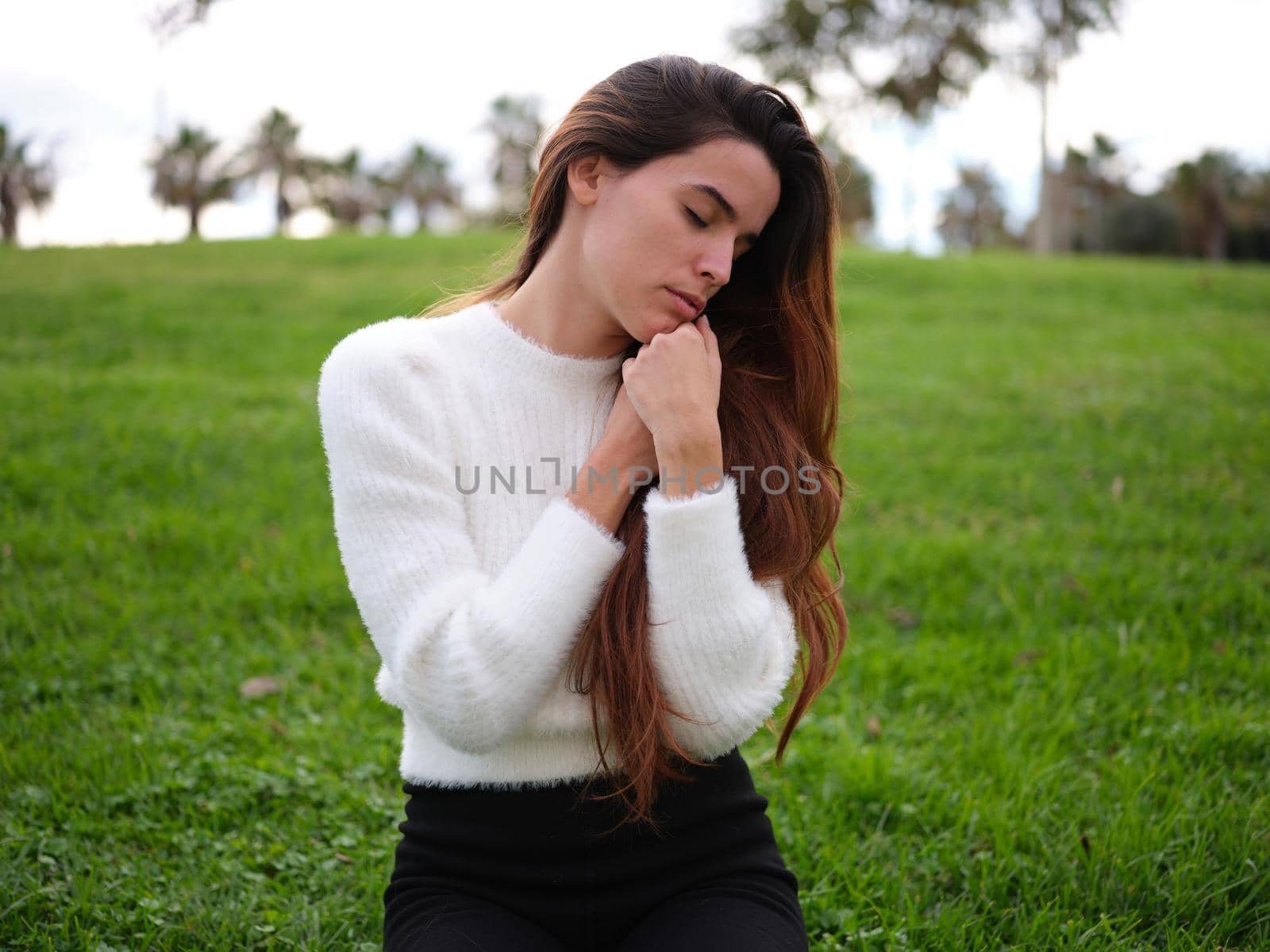 Front view of a caucasian young woman relaxing in the park with her hands folded on her chest and her eyes closed. Concept of emotions.