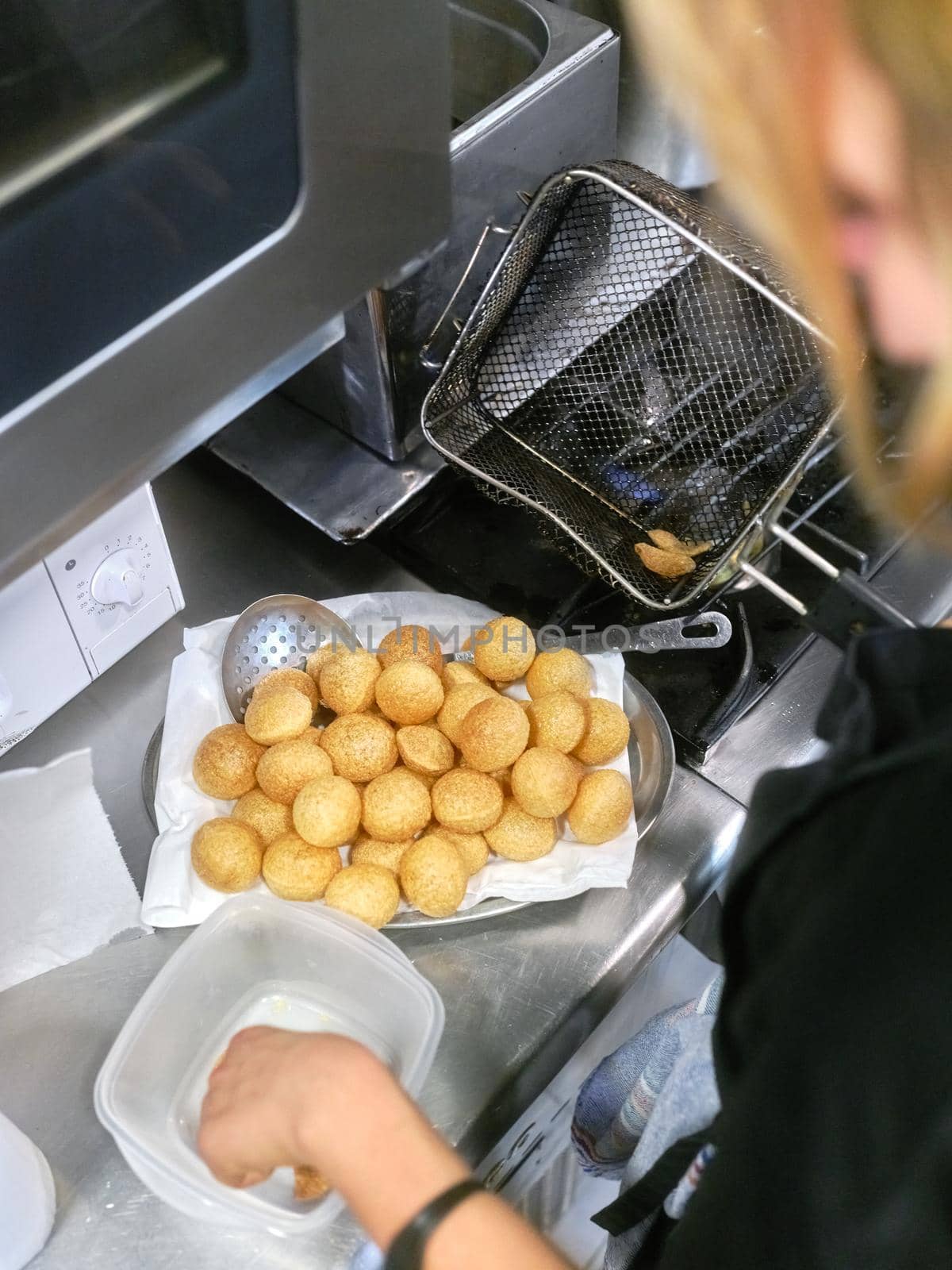 Vertical top view photo of a cook frying fritters with an electric fryer