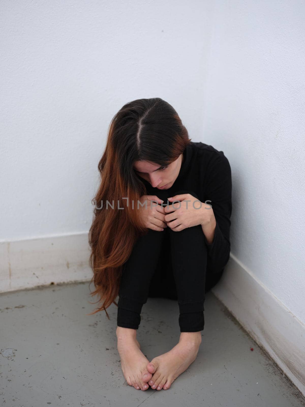 A young woman in the corner of a room dressed in black barefoot looking down in desolation. by WesternExoticStockers