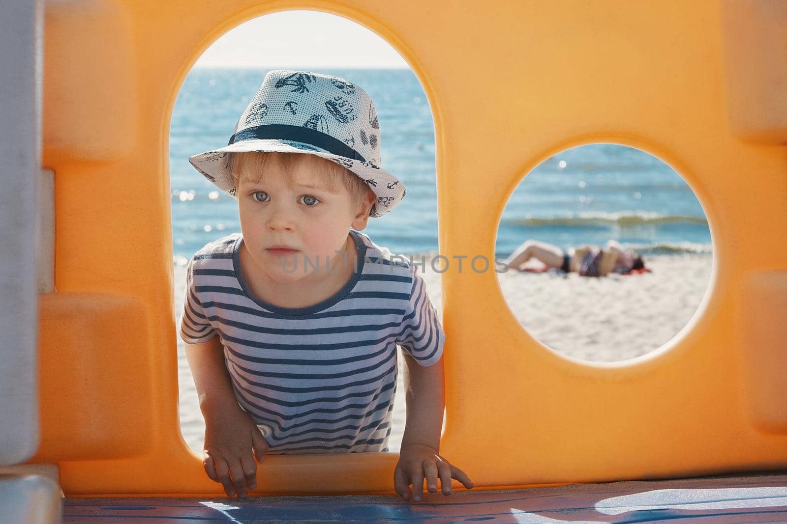 Portrait of a boy with a hat, framing with orange arche and a circle, beach in the background. by Lincikas