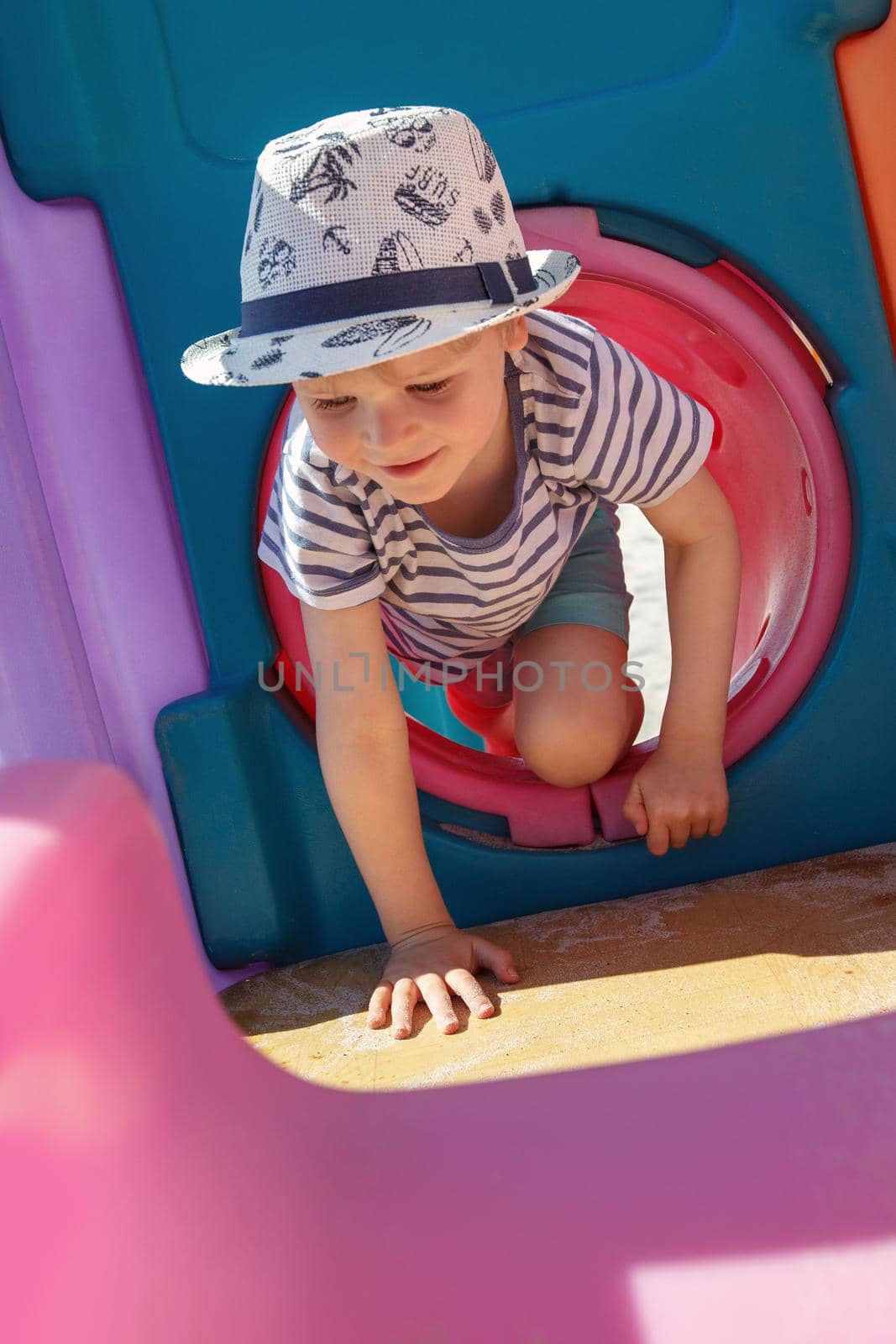 The little boy plays in a colorful, plastic playroom, he performs crawl in tunnel exercises