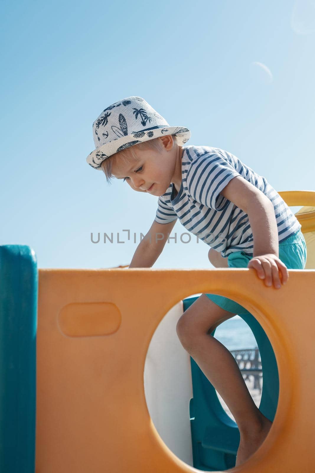 The little boy climbs up on the beach playground while playing he is very focused and careful