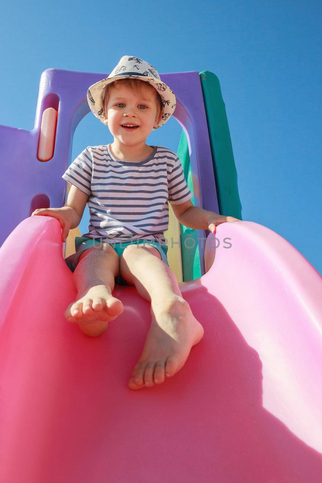 Happy child playing with pink slide on blue sky background. Playtime concept