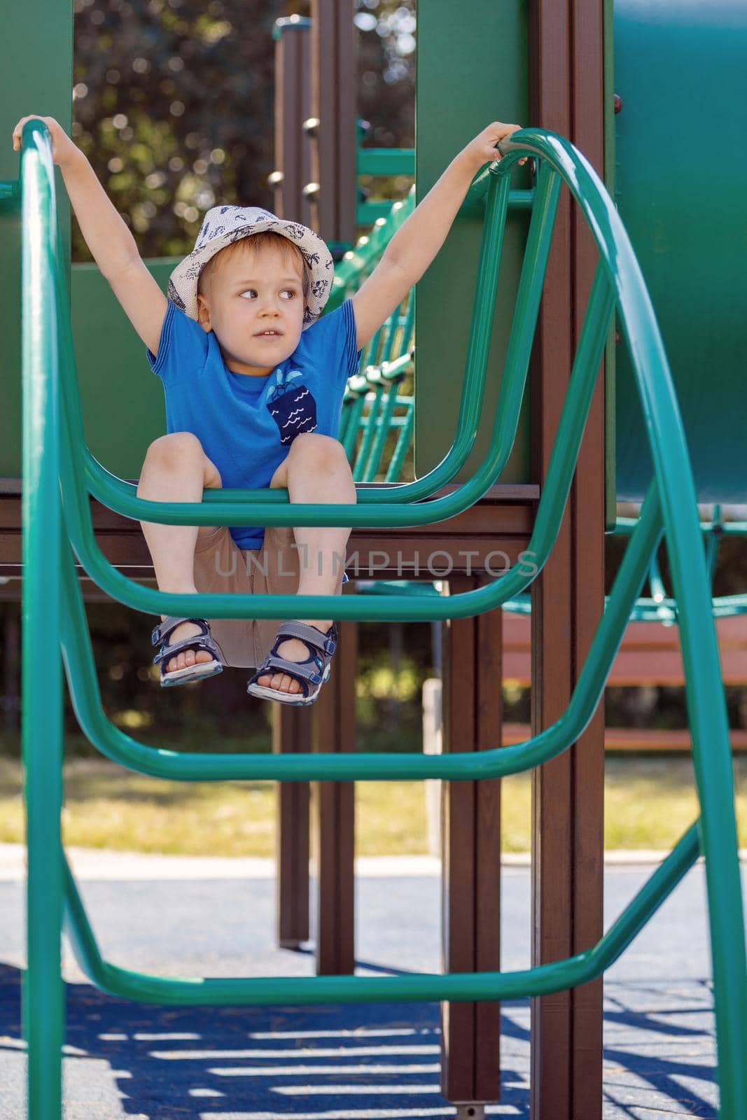 Happy 3 year boy climbing and playing at the children playground outdoor city park. The child hung on a green tubular ladder.