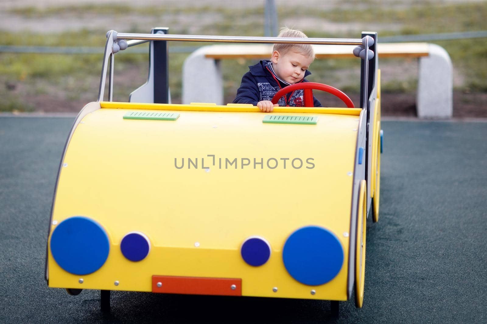 A little boy plays and drives a yellow big car on a playground. The child's interest and involvement in the play process