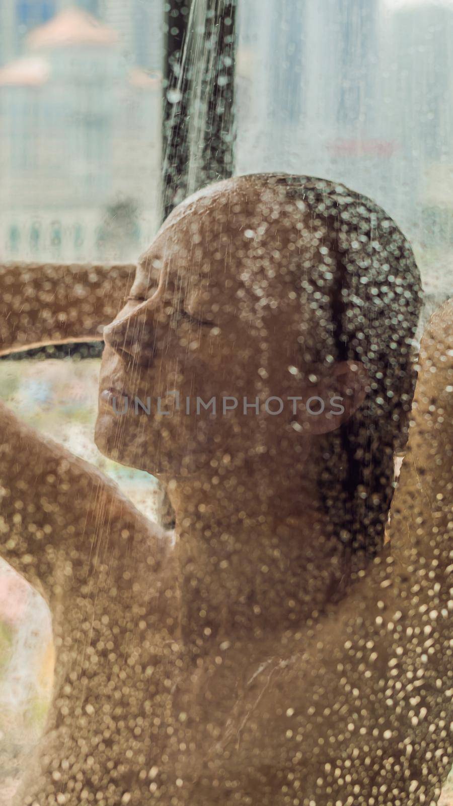 Beautiful woman in the shower behind glass with drops on the background of a window with a panoramic view of the city VERTICAL FORMAT for Instagram mobile story or stories size. Mobile wallpaper by galitskaya