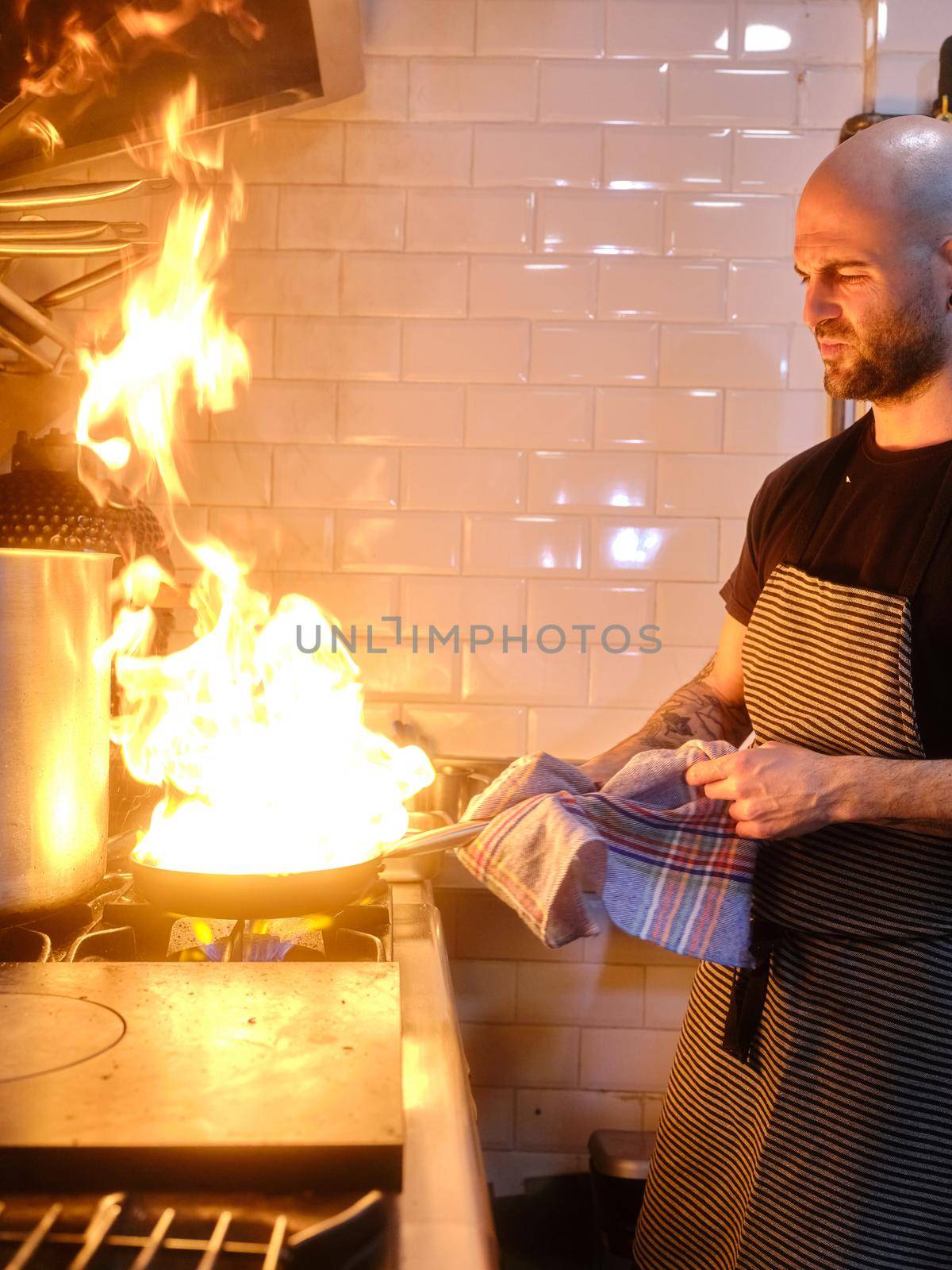 Vertical photo of a pan full of flames while a chef cook flaming the food in a restaurant