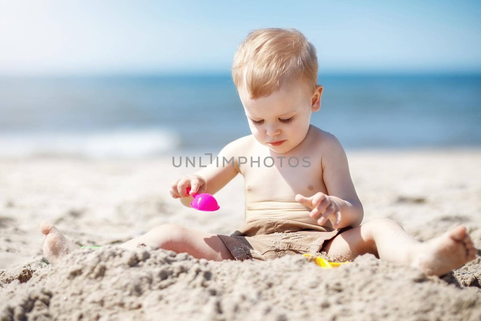 European two year old toddler boy playing with beach toys on beach. The child is very focused on wanting to create something out of sand