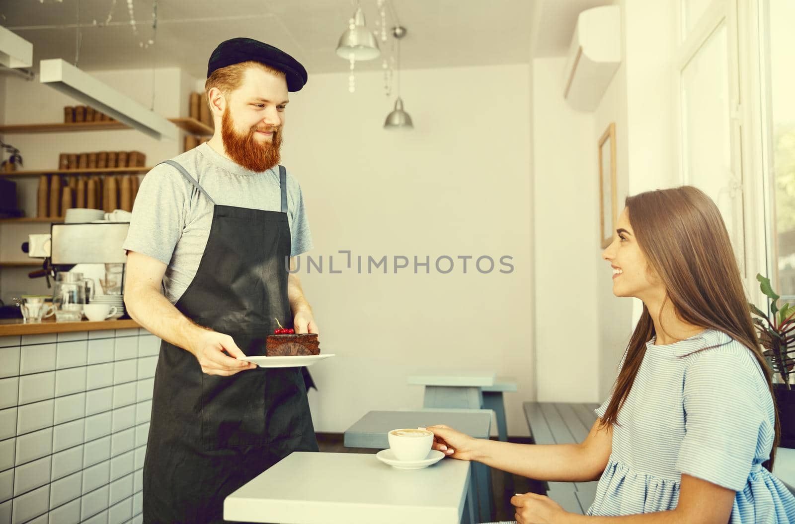 Coffee Business Concept - Waiter or bartender giving chocolate cake and talking with caucasian beautiful lady in blue dress at Coffee shop