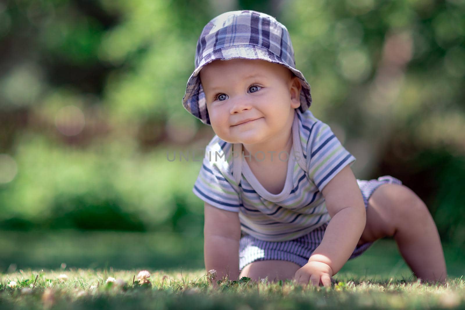 Baby with nice blue cap crawling on the green grass in the garden