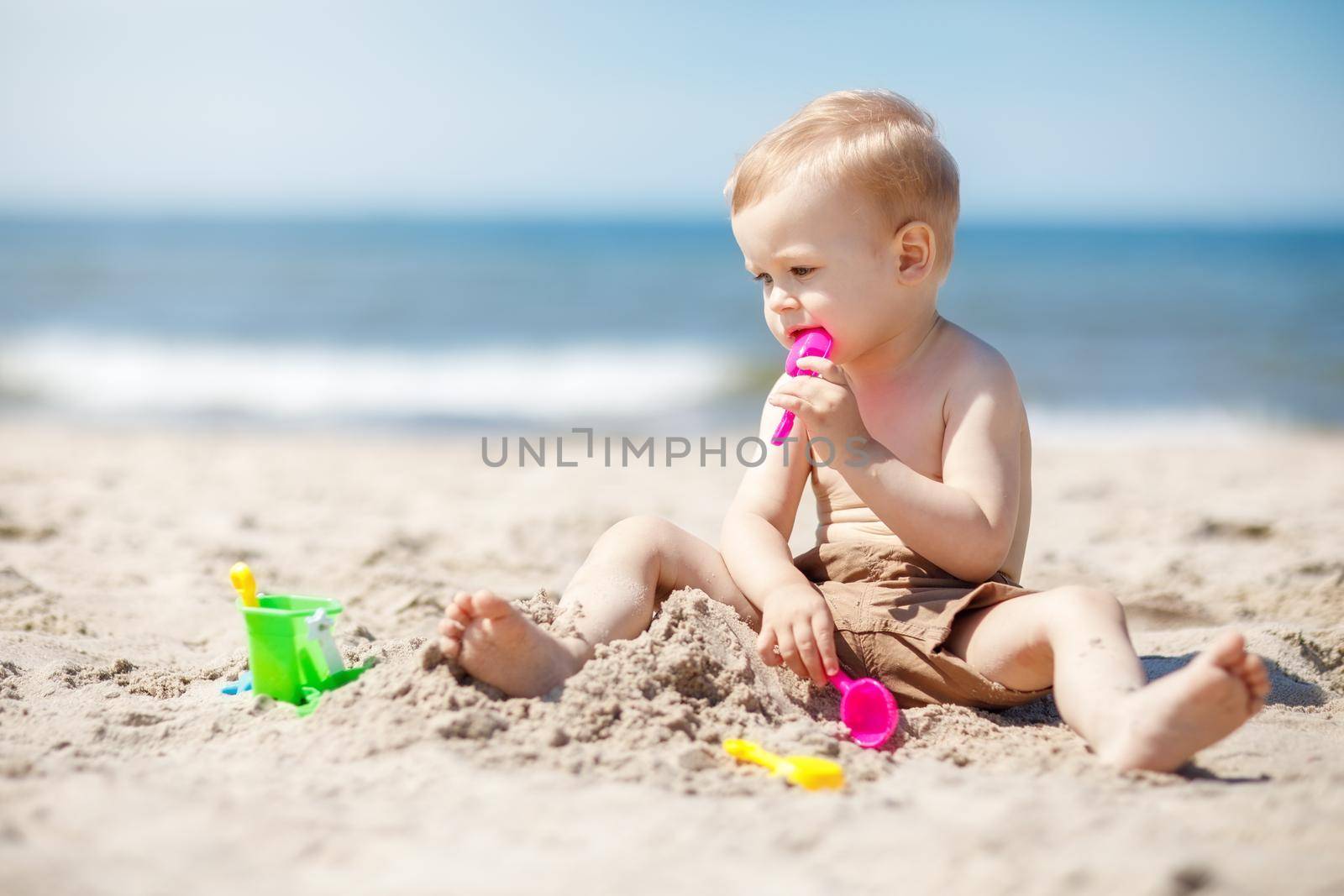 Little boy playing on the beach with sand beach toys. The boy is thinking about what to make of sand