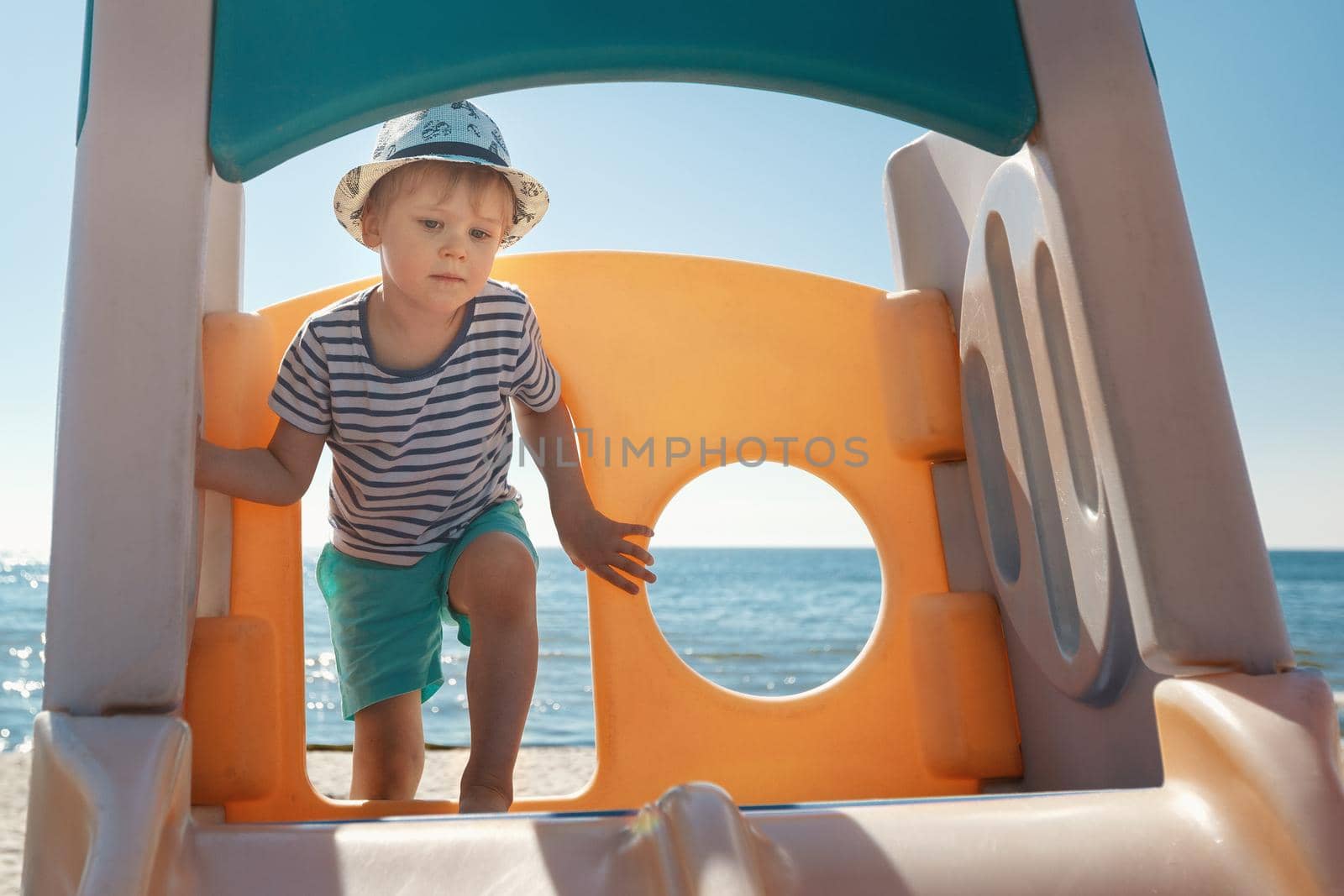 The boy climbs up to the orange children's slide on the beach