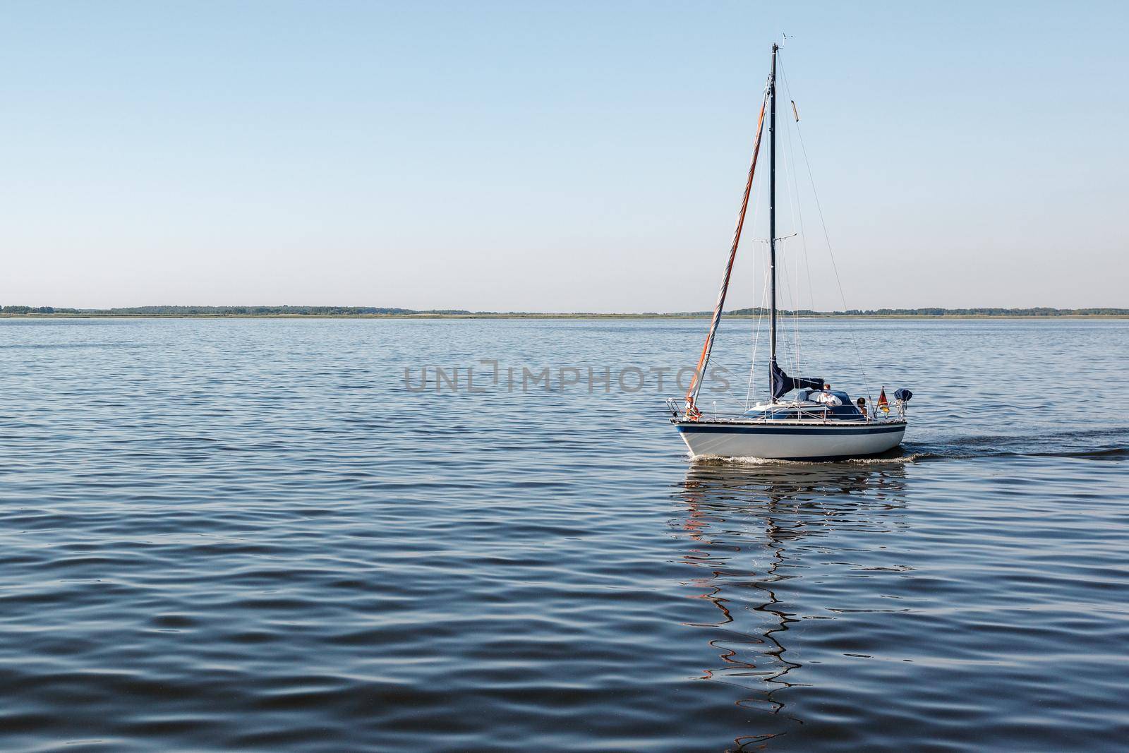 A quiet summer day and a lonely yacht with lowered sails and the German flag in the lagoon