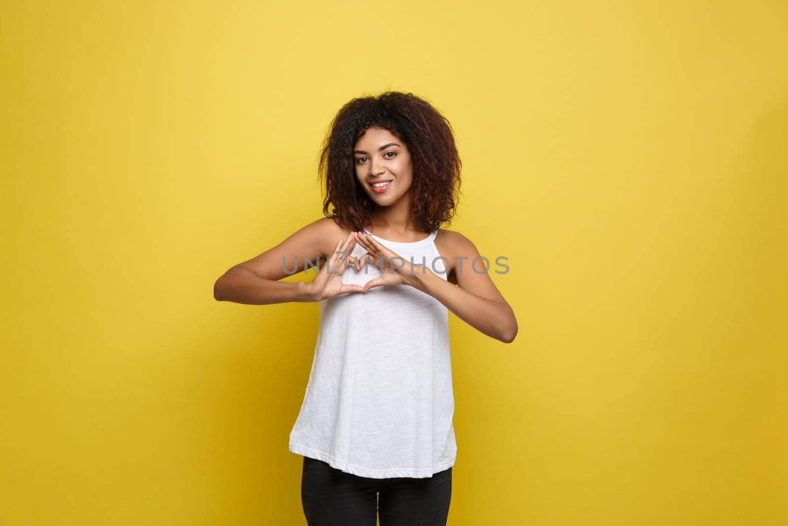 Isolated portrait of beautiful African American make heart symbol by hands. Yellow studio background. Copy Space. by Benzoix