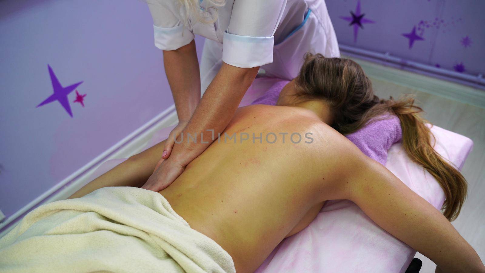 Young unrecognizable woman gets professional back massage in spa salon. Beautiful naked lady with perfect skin gets relaxing massage. Concept of luxury professional massage by Matiunina