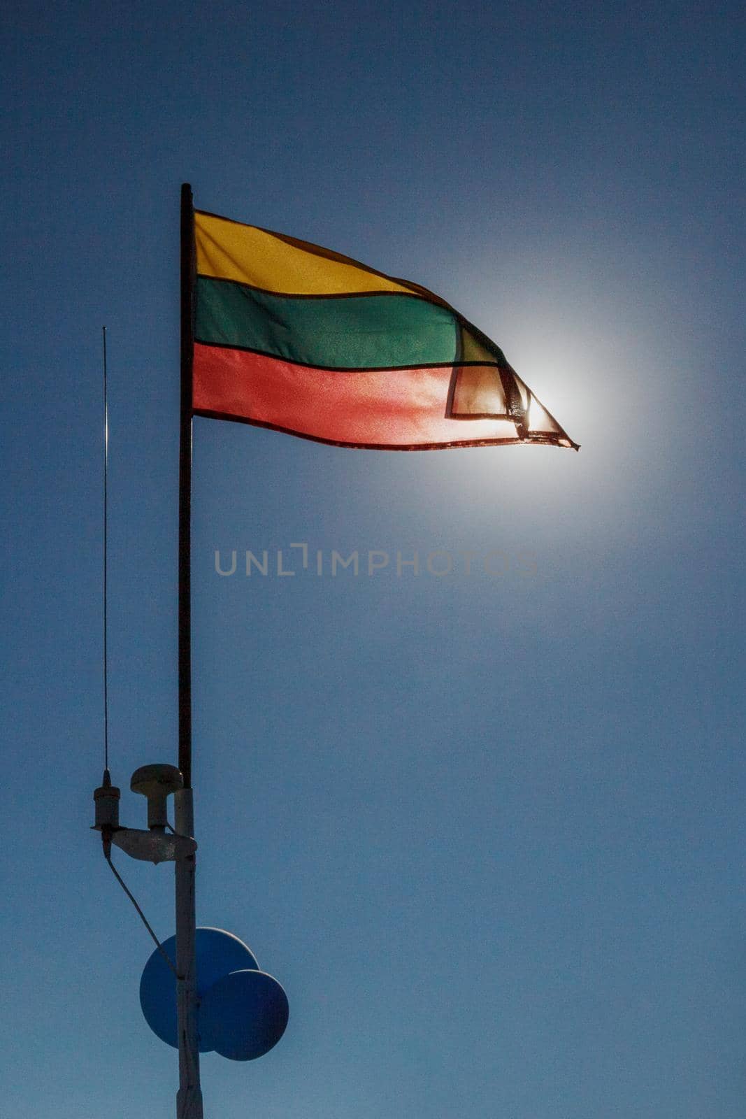The Lithuanian flag is raised on the ship's mast, it is lit by the sun against a background of blue sky. Vertical photo