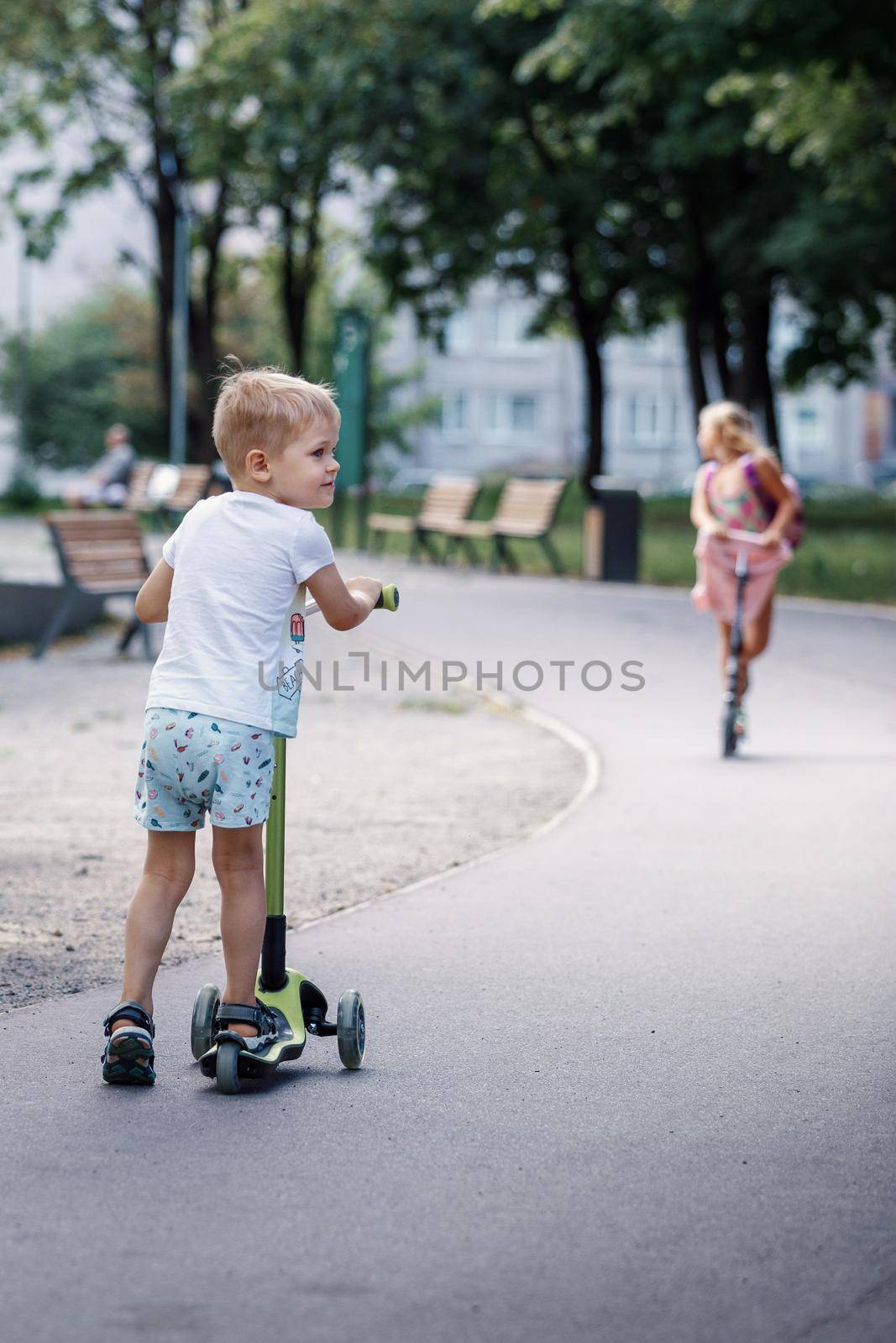 Child on kick scooter in park. A boy is riding on the kick scooter in a park. The concept of a healthy lifestyle. Kids sport.