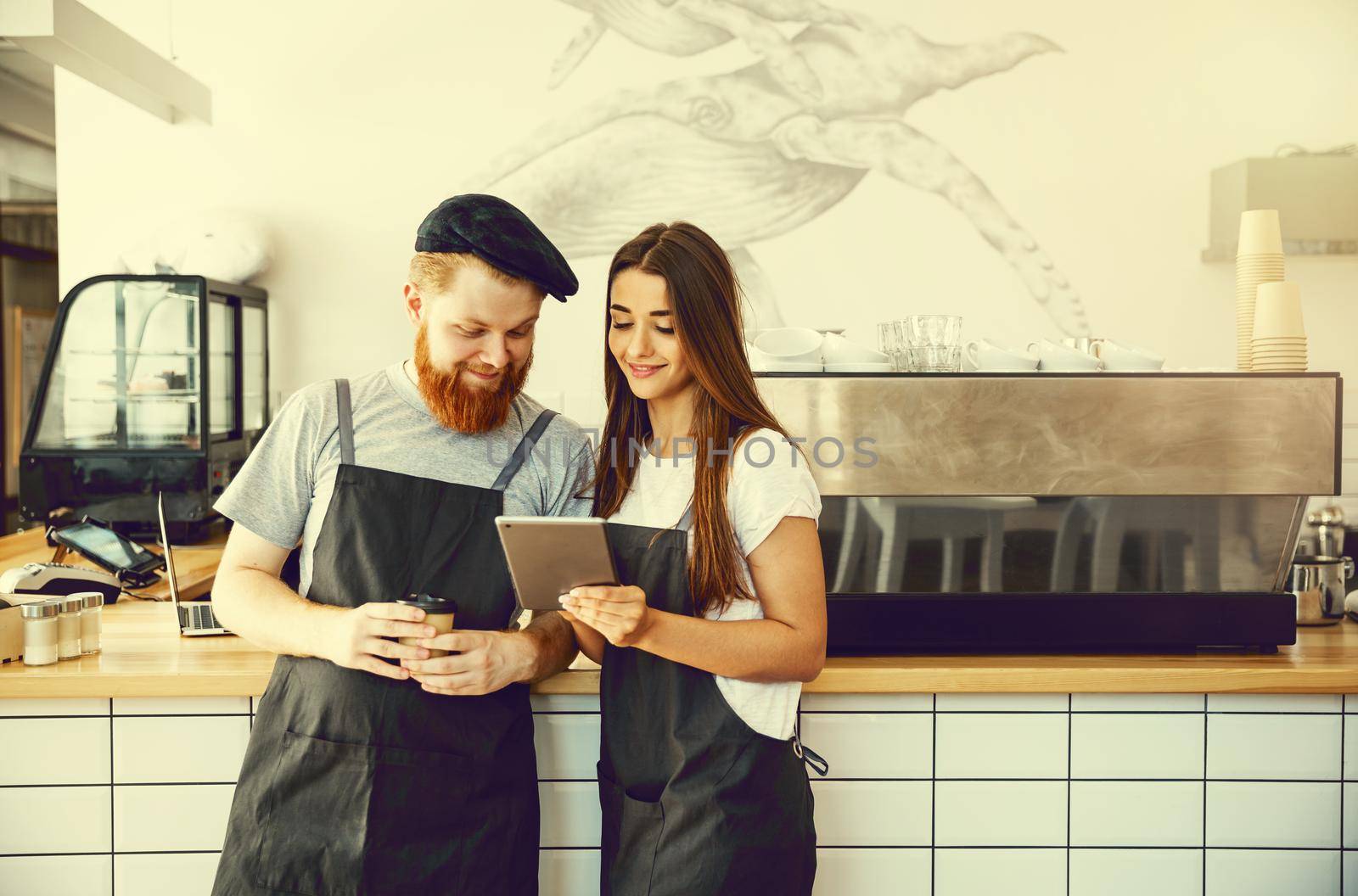 Coffee Business Concept - Cheerful baristas looking at their tablets for online orders