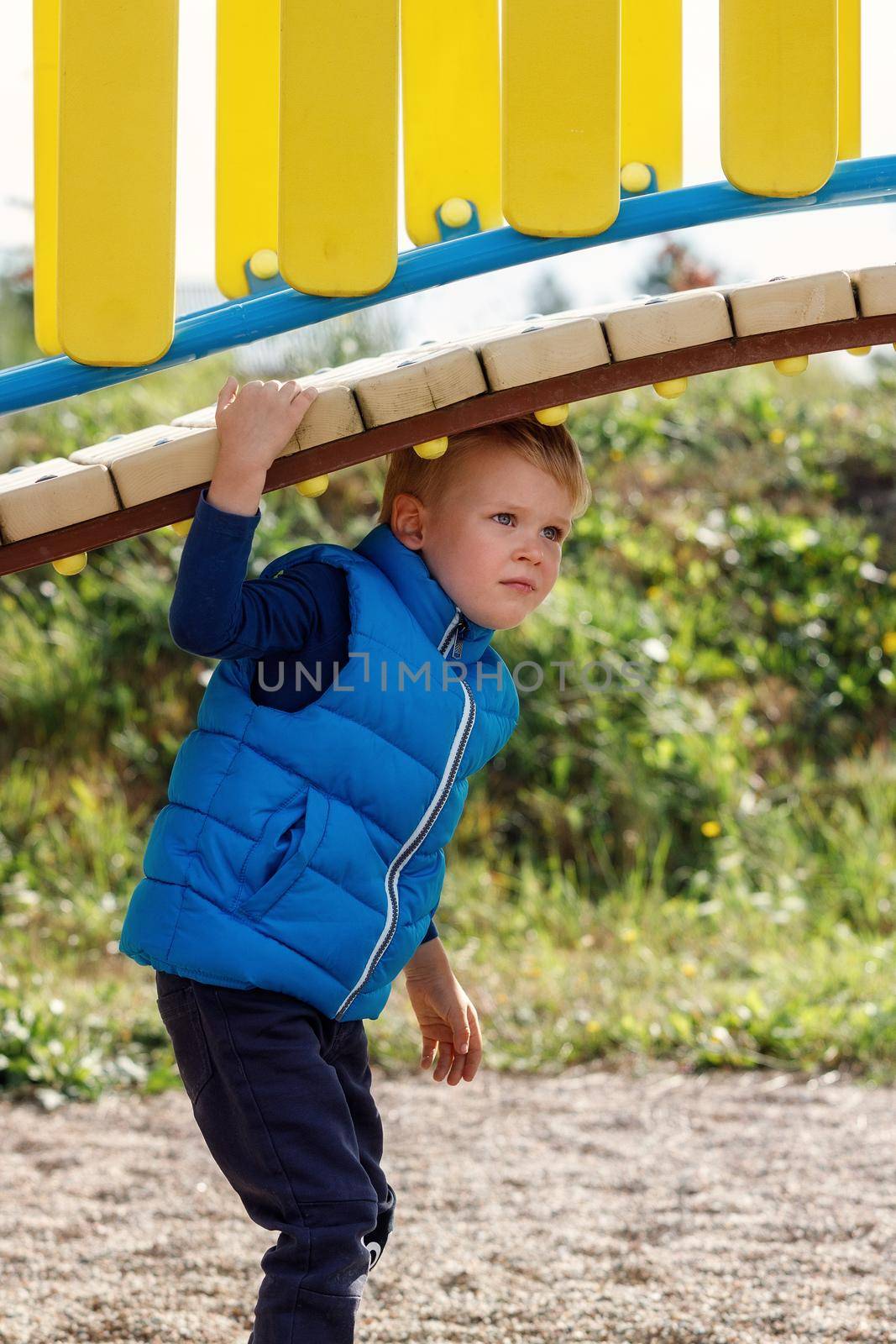 A little cute boy plays under a beautiful, curved bridge on a colorful playground. Vertical photo by Lincikas