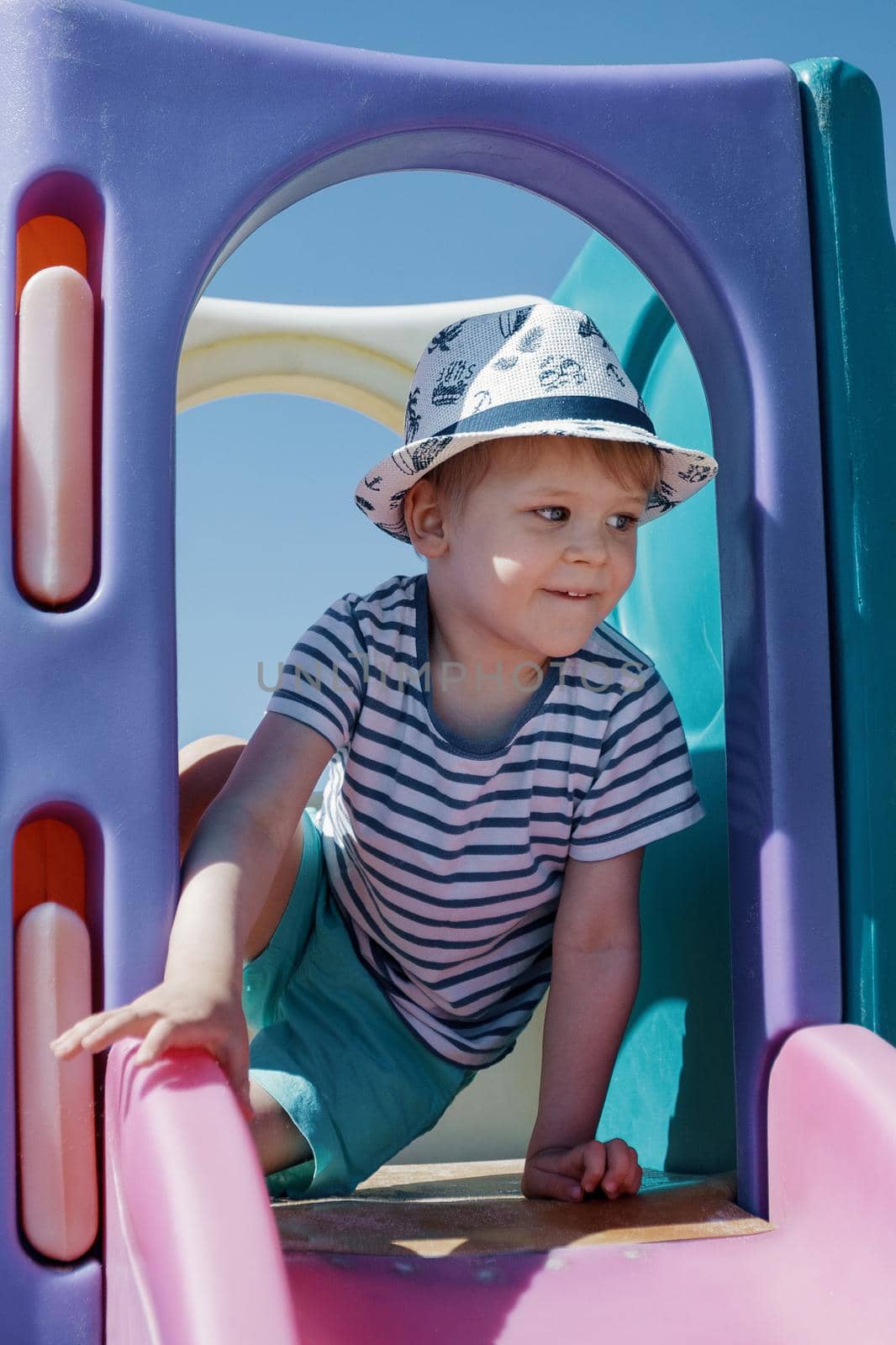 A little boy in a hat and a striped sailor shirt, go through through an arch on a beach playground