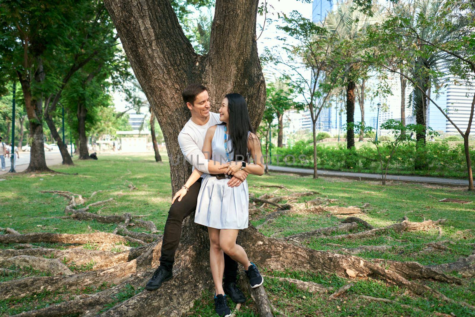 Multiethnic couple in love embracing while leaning against a tree together by WesternExoticStockers