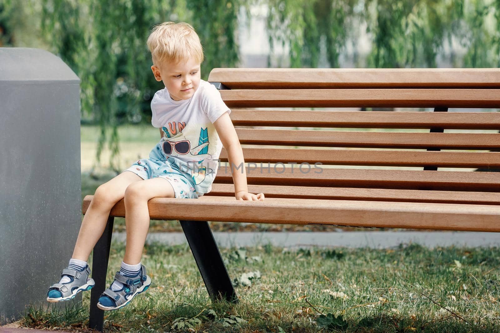 Small child plays in park, climbs onto bench. Kid is sitting on a park bench.