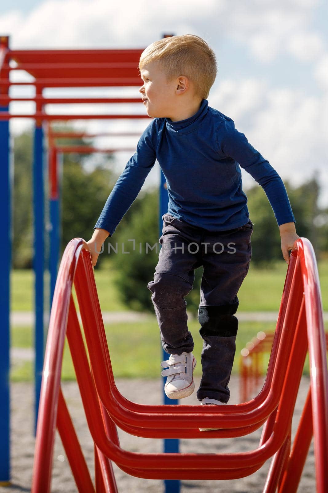 A little boy is climbing and hanging on a metal ladder in the form of an arc in the playground.