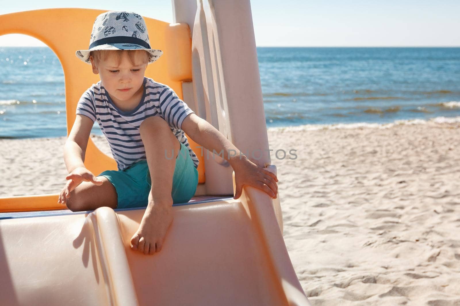The boy is getting ready to slide down from the beach slide, sea background