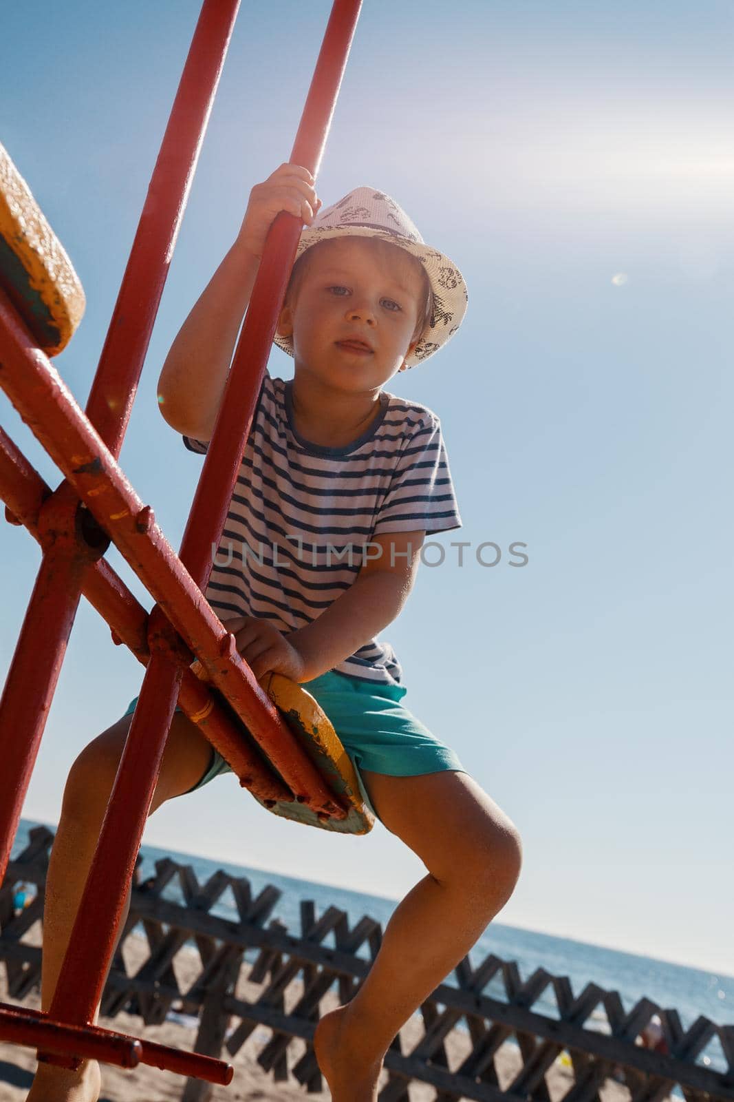 Little boy on a balance swing, in a beach background. by Lincikas