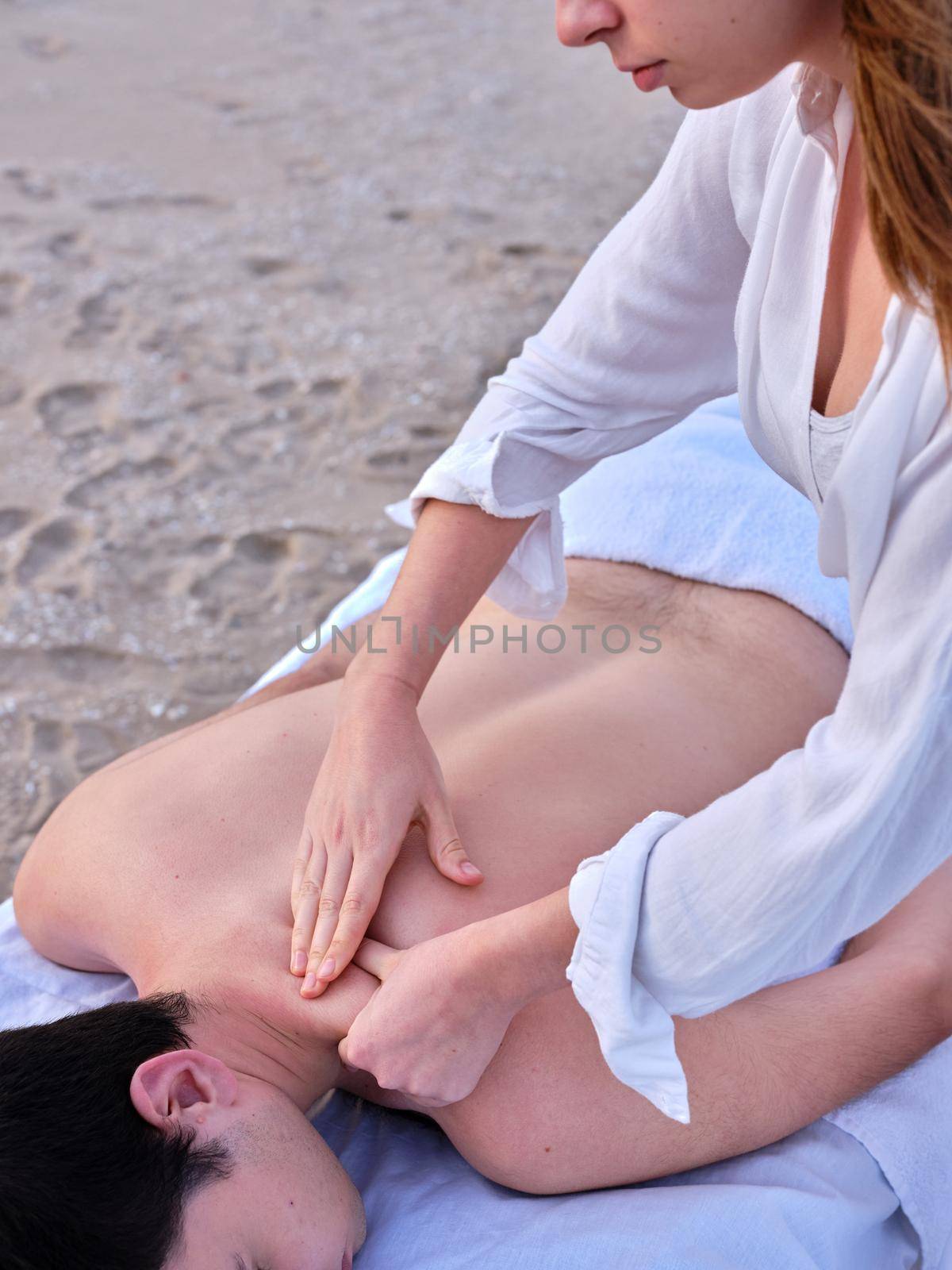 A young chiromassage therapist doing a shoulder massage to a young man on a beach in Valencia. by WesternExoticStockers