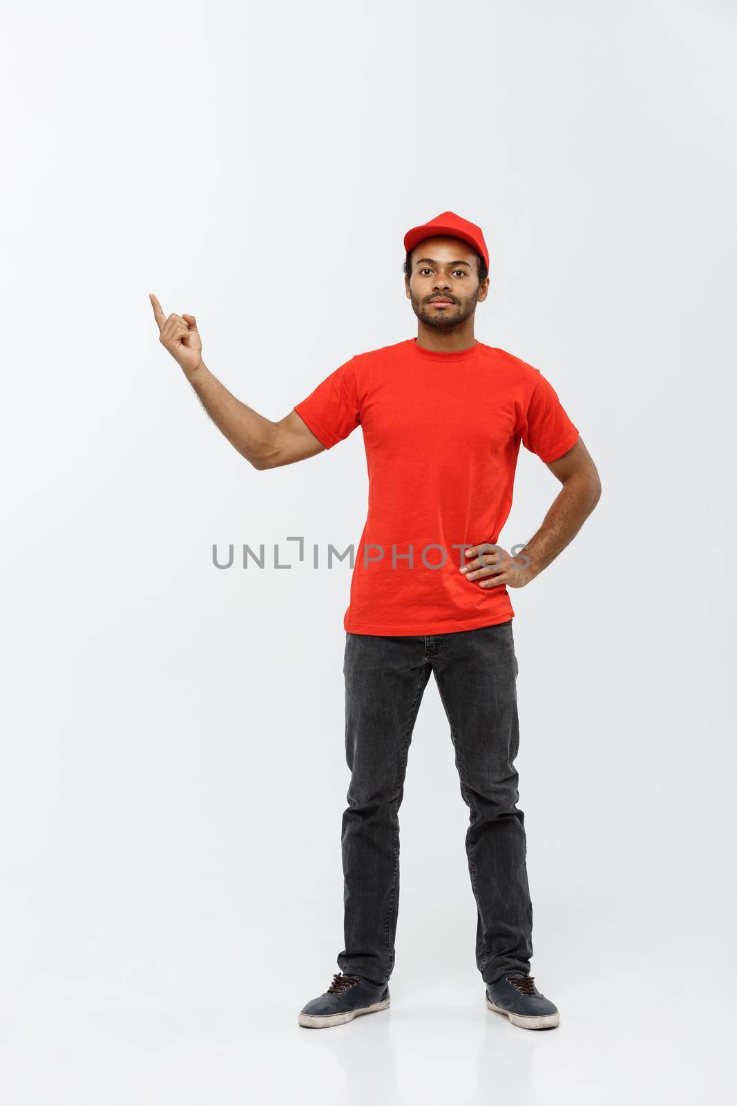 Delivery Concept - Portrait of Happy African American delivery man pointing hand to present something. Isolated on Grey studio Background. Copy Space. by Benzoix