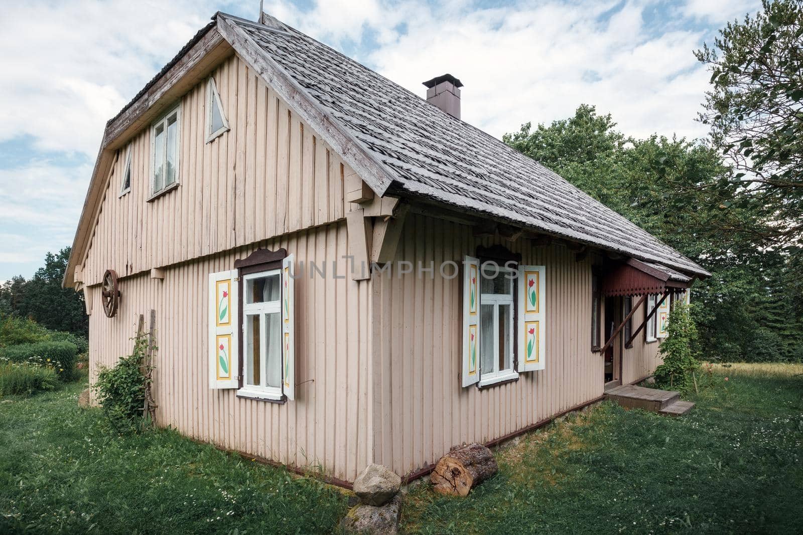 Old traditional wooden house with windows and shutters, rear view. An old carriage wheel is hung on the wall, the roof is covered with wooden tiles.