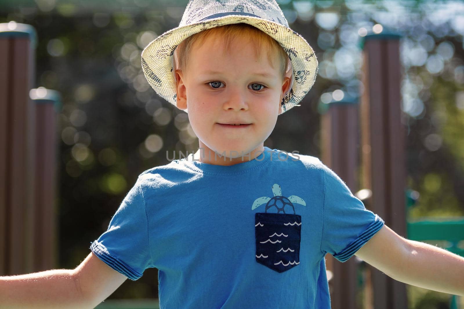 Adorable European boy in blue shirt and hat, smiling, happy playing in a park. by Lincikas