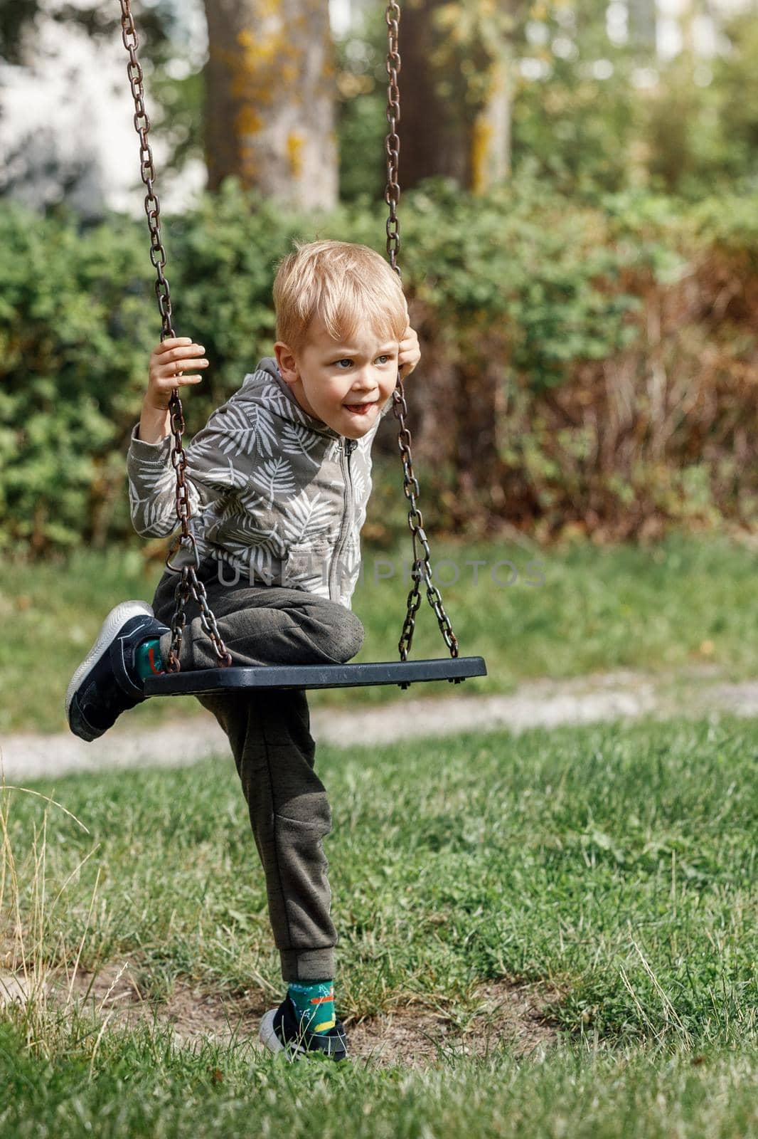 The blond boy plays with a chain swing as he tries to climb on it without his parents help. by Lincikas