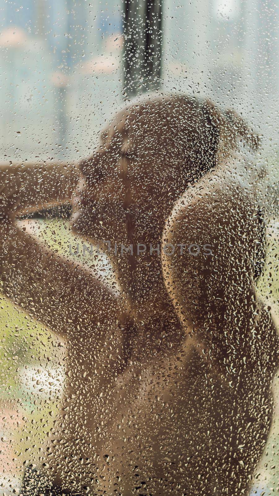 Beautiful woman in the shower behind glass with drops on the background of a window with a panoramic view of the city. VERTICAL FORMAT for Instagram mobile story or stories size. Mobile wallpaper