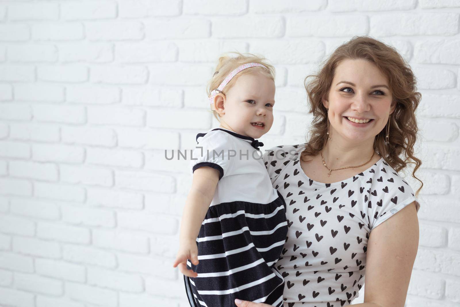 Mother holds and having fun her child with hearing aids and cochlear implants on white brick wall with copy space and place for advertising . Deaf and innovating medicine technologies concept by Satura86