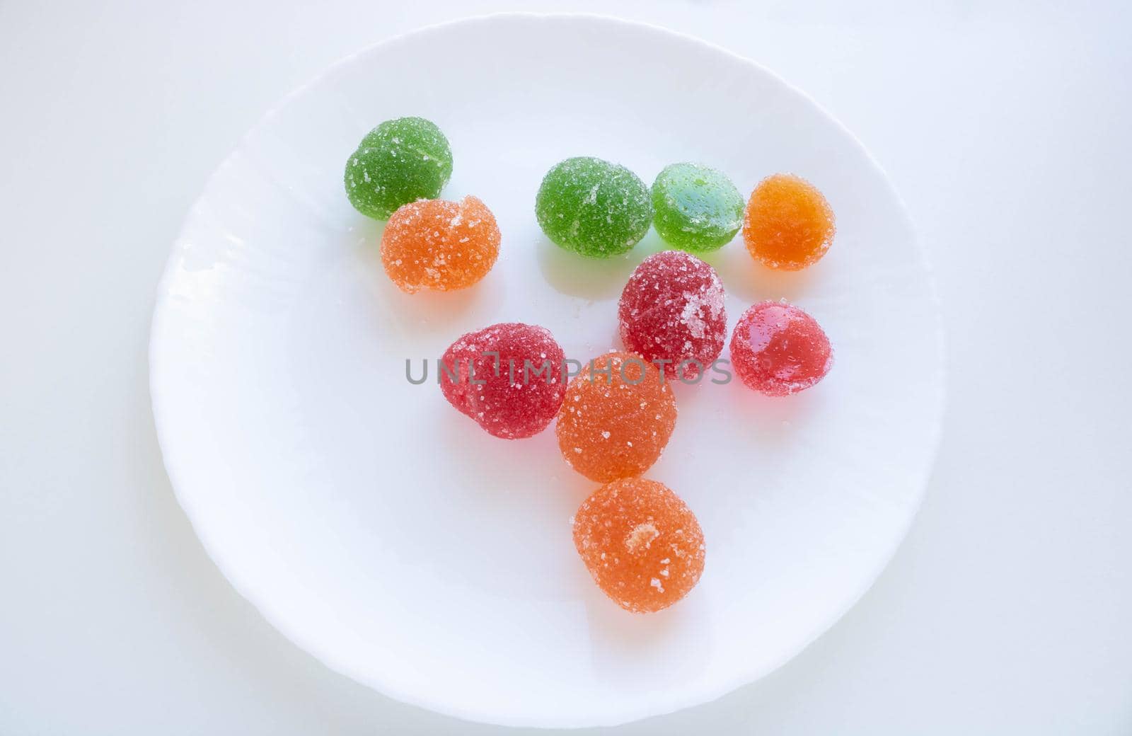A pile of red, green and yellow jelly cubes on a white plate on a white background
