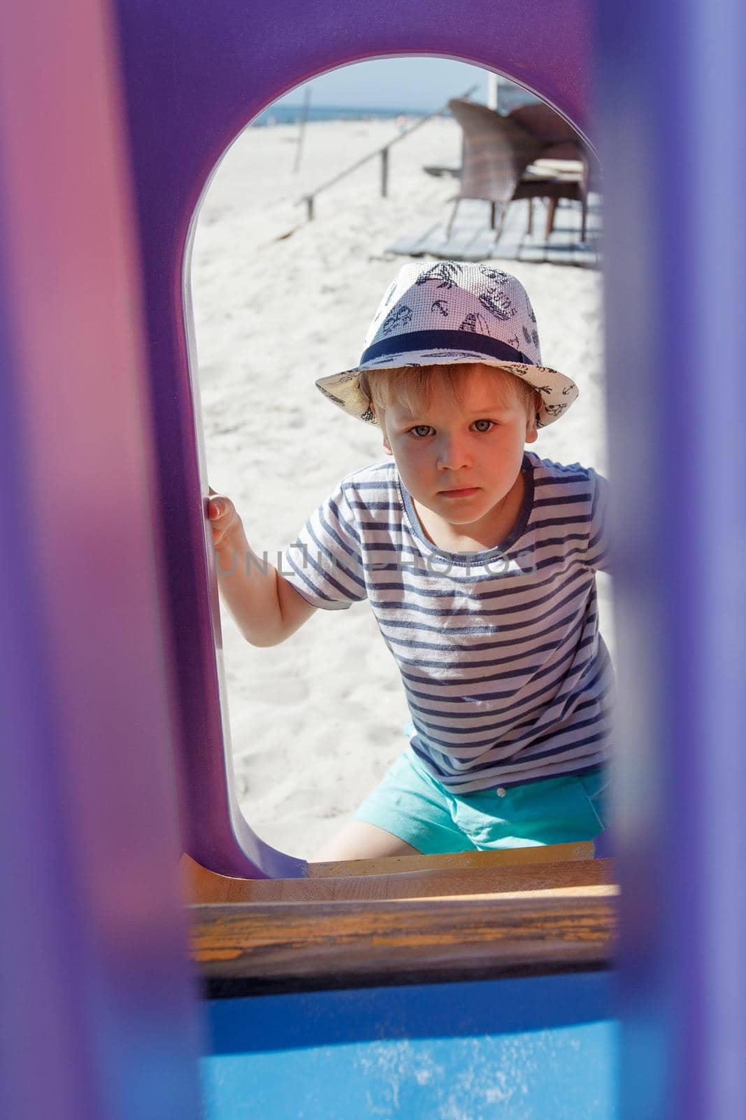 A portrait of a boy in the background of a beach playground. Framing a purple plastic arch. by Lincikas