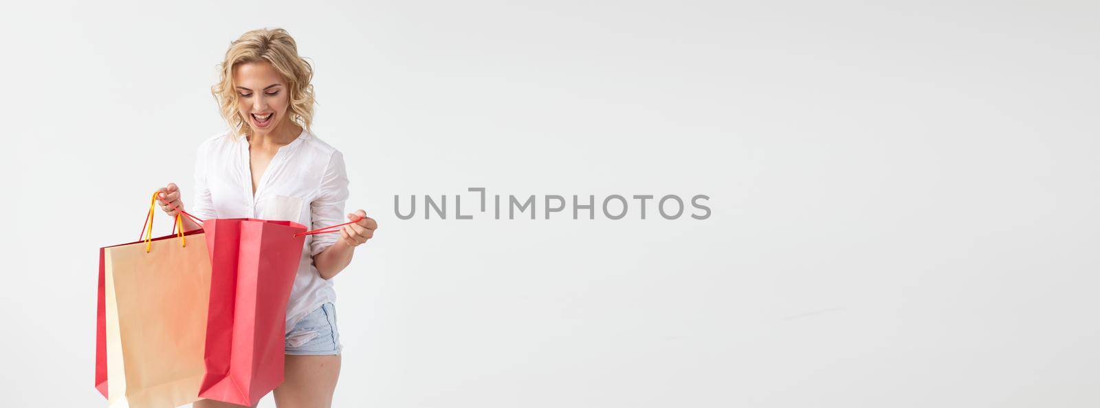 Charming young joyful blonde woman holds in her hands bags with a new clothing posing on a white background. Shopping concept. Copyspace