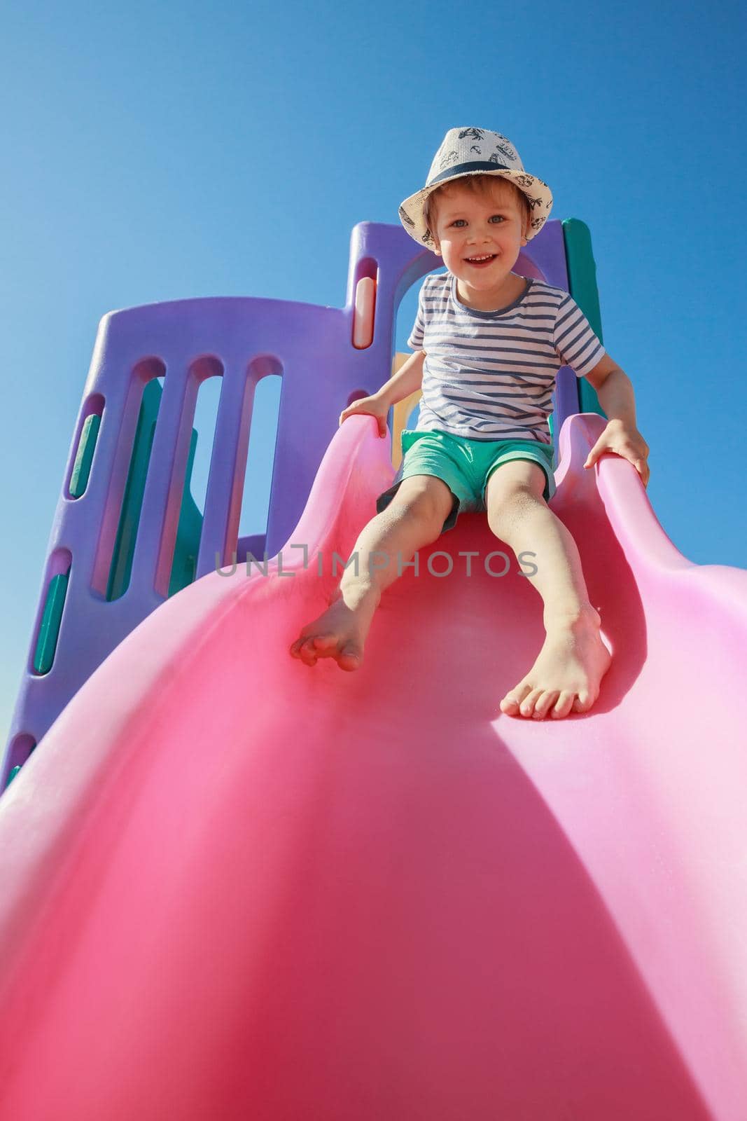 Happy kid playing slide at the playground under the sunlight in summer