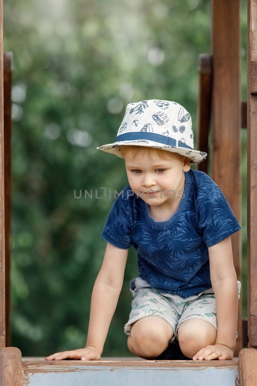 Portrait of a cute boy with a white hat and a blue shirt at the top of the playground.