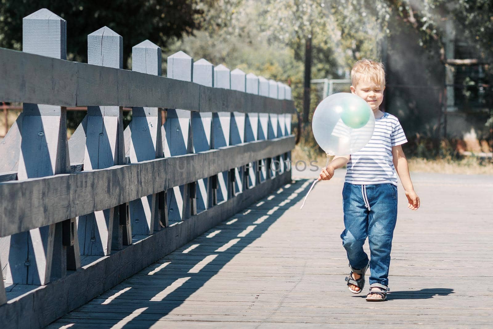 A child walks across a bridge on a sunny summer day in the city, carrying a hot air balloon.