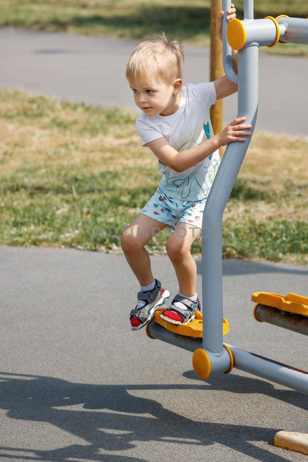 The little boy is playing on an outdoor gym equipment.