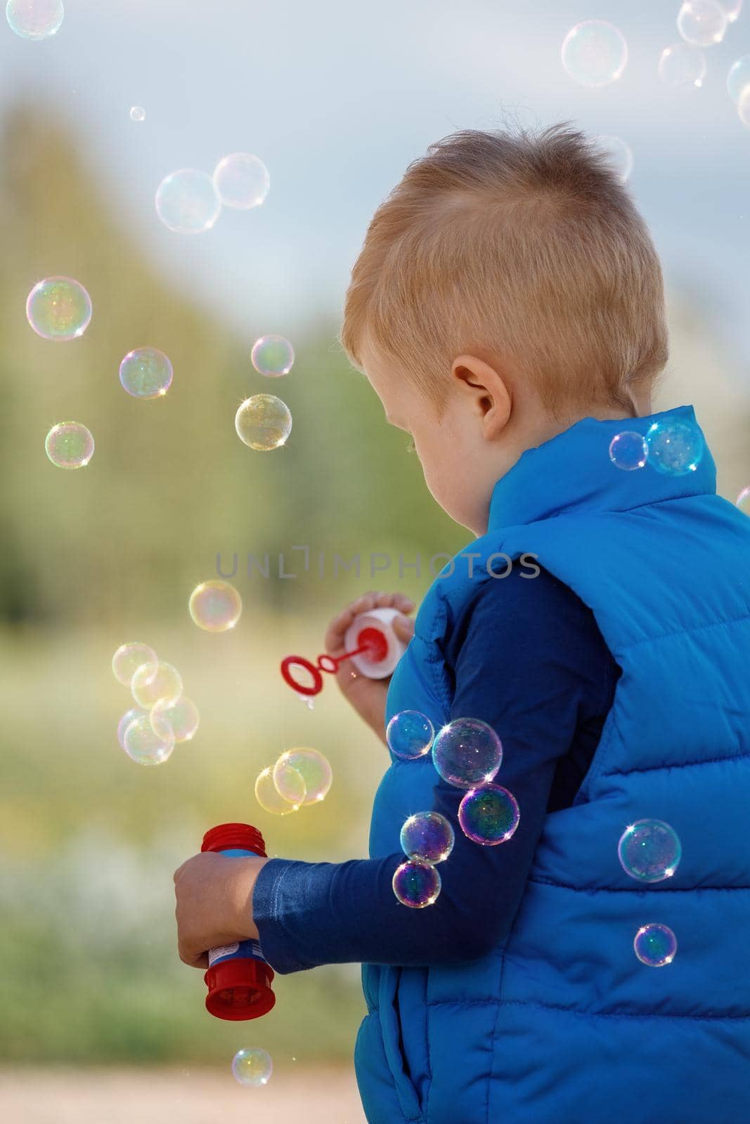A little boy blows soap bubbles. Games with children in nature, in the fresh air in summer. A child plays with soap bubbles in the street.
